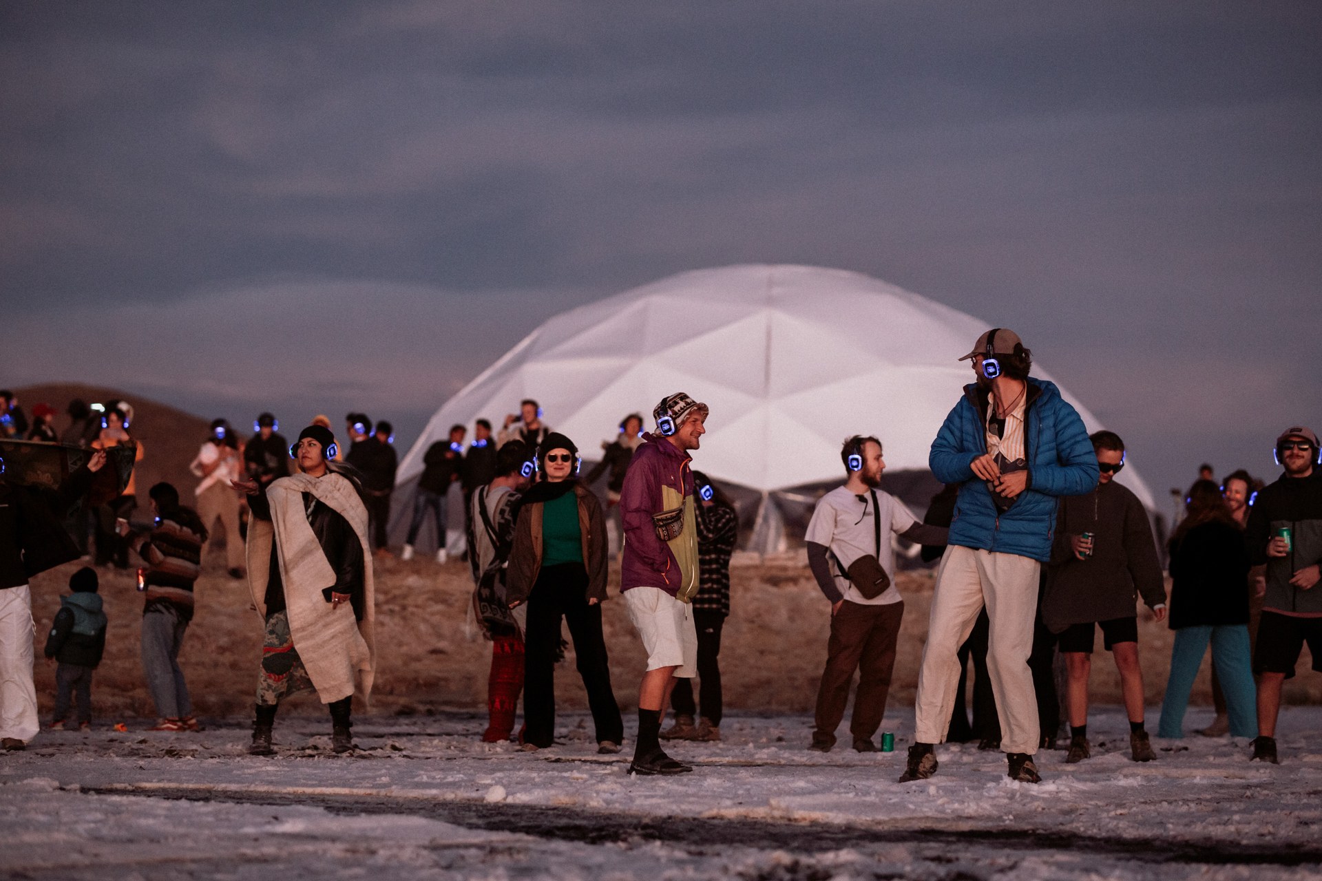 Festival guests dancing on the salt flats beside an illuminated dome